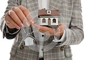 Real estate agent holding house model and key on white, closeup