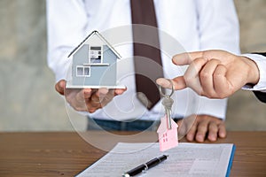 Real estate agent holding house model and keys,  customer signing contract to buy house, insurance or loan real estate