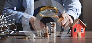 Real estate agent holding magnifying glass on coins and house model