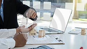 Real estate agent holds house keys for clients after signing contract in office, real estate concept with house model and laptop