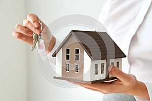 Real estate agent with house model and key on light background, closeup