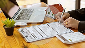 A real estate agent introduces clients to a home layout with contract documents and a laptop and dollar bill on the table. Custome