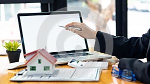 A real estate agent introduces clients to a home layout with contract documents and a laptop and dollar bill on the table. Custome