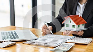 A real estate agent introduces clients to a home layout with contract documents and a laptop and dollar bill on the table. Custome