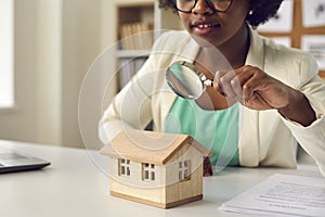 Real estate agent with a magnifying glass looking at a little house on her table