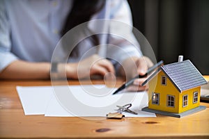 real estate agent places miniature model home on desk inside real estate sales office to allow customers to use model home as