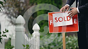 Real estate agent puts sold inscription on for sale signboard, successful deal