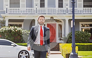 Real estate. Agent ready to sell home. Businessman standing outside a modern house. Dream home.