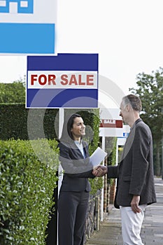 Real estate agent shaking hands with man beside for sale signs