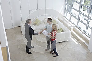 Real Estate Agent Shaking Hands With Man By Woman In New Home