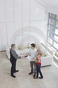 Real Estate Agent Shaking Hands With Man By Woman In New Home