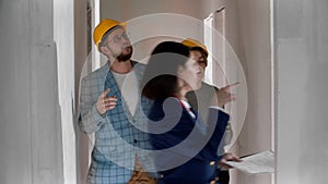 A real estate agent showing a new draft apartment to a young married couple in helmets - looking around