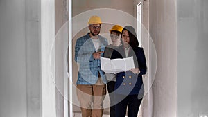 A real estate agent showing a new draft apartment to a young married couple in helmets - looking at the paper