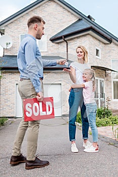 real estate agent with sold sign giving key to young woman