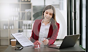 Real estate agent worker working with laptop and tablet at table in office and small house beside it