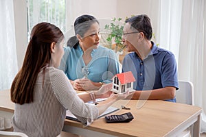 Real estate agent young asian woman talking with elderly couple and explaining mortgage or buying home insurance.