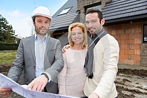 Real estate agent and a young couple in front of future home