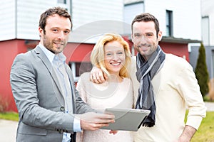 Real estate agent and a young couple in front of their next home