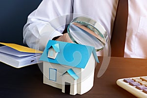 Real estate assessment. Man looking through magnifying glass on model of house.