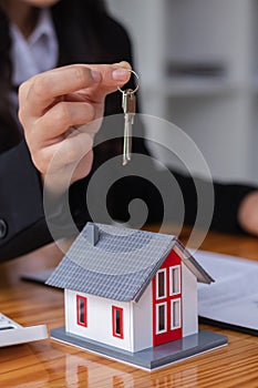 The real estate broker is handing over the house keys to the customer after signing the contract with the dealer in office.