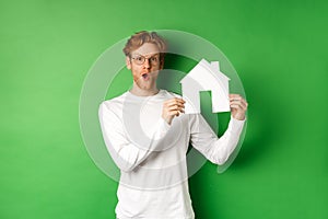 Real estate and buying property concept. Surprised young redhead man showing paper house model and looking amazed