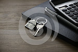 Real estate concept. Selective focus of key and house keychain, calculator, pen and notebook on wooden background
