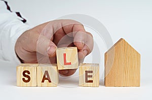 On a white surface there is a model of a house, next to it a man has placed cubes with the inscription - SALE