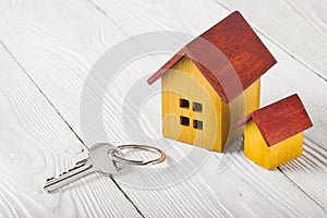 Real estate concept with wooden house and key on white wooden background. Idea for real estate concept, personal property and fami