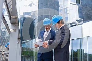 Real estate developers in helmets. New office construction. Confident business men and architect talking in front of