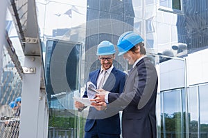 Real estate developers in helmets. New office construction. Confident business men and architect talking in front of