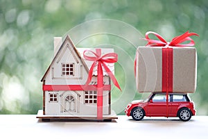 Real estate and Gift new home concept,Model house and gift box with red ribbon on miniature ca on green background.