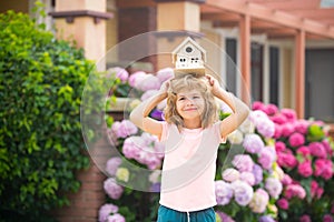 Real estate, housing and family concept. Funny kid holding toy wooden house near new home.