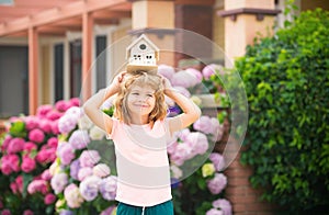 Real estate, housing and family concept. Funny kid holding toy wooden house near new home.