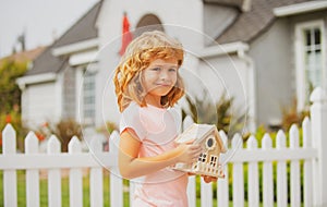 Real estate, housing and family concept. Kid holding toy wooden house near new home.