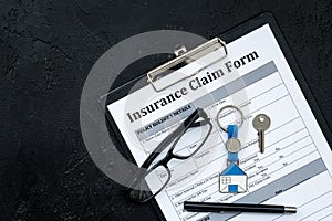 Real estate insurance. Insurance claim form near house keychain on black background top view copy space