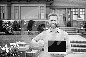 Real estate manager. Happy businessman standing outside near his new home. Suburban house. Young man holding laptop
