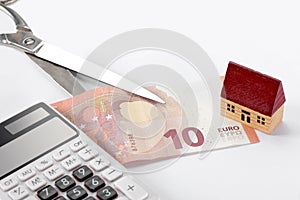 Real estate and mortgage concept: toy house, euro bill, scissors and a calculator on white background with copy space for