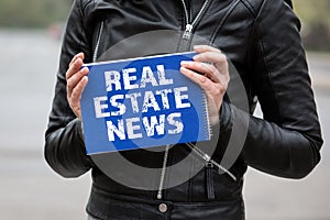 REAL ESTATE NEWS. Woman holding blue notebook with text