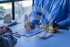 Real estate office, home sales agent sitting at desk with contract documents and house