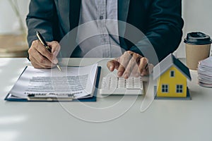 Real estate office, home sales agent sitting at desk with contract documents and house