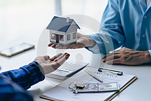 Real estate office, home sales agent sitting at desk with contract documents and house