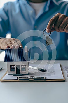 Real estate office, home sales agent sitting at desk with contract documents and house