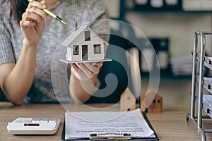 Real estate office, home sales agent sitting at desk with contract documents and house