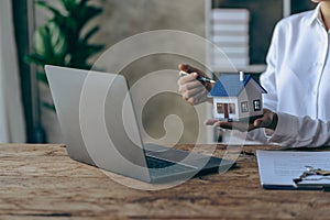 Real estate office, home sales agent sitting at desk with contract documents and house