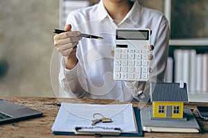 Real estate office, home sales agent sitting at desk with contract documents and house