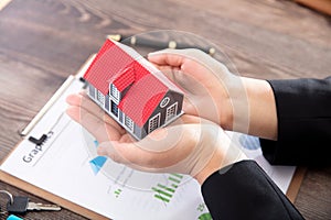 Real estate practitioners hold small house models and related documents and coins