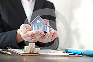 Real estate practitioners hold small house models and related documents and coins