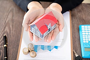 Real estate practitioners hold small house models and related documents and coins