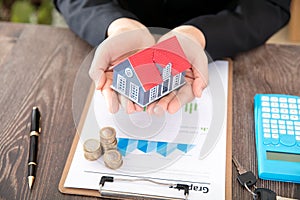 Real estate practitioners hold small house models and related documents and coins