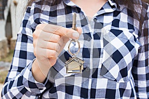 Real estate and property concept - Close up of woman is holding house keys on house shaped keychain in front of a new
